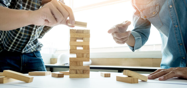 Dois homens tentando equilibrar uma torre com jogo de madeiras para não deixar cair