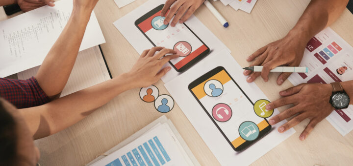 grupo de pessoas ao redor de uma mesa projetando ideias em um papel com canetinhas e desenhos