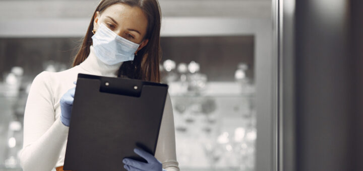 Product Owner mulher usando máscara realizando anotações em uma prancheta preta com luvas ortopédicas azuis