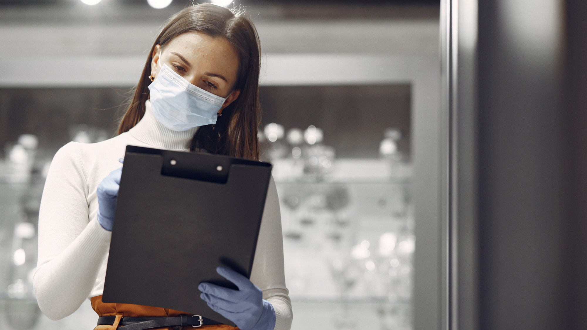 Product Owner mulher usando máscara realizando anotações em uma prancheta preta com luvas ortopédicas azuis